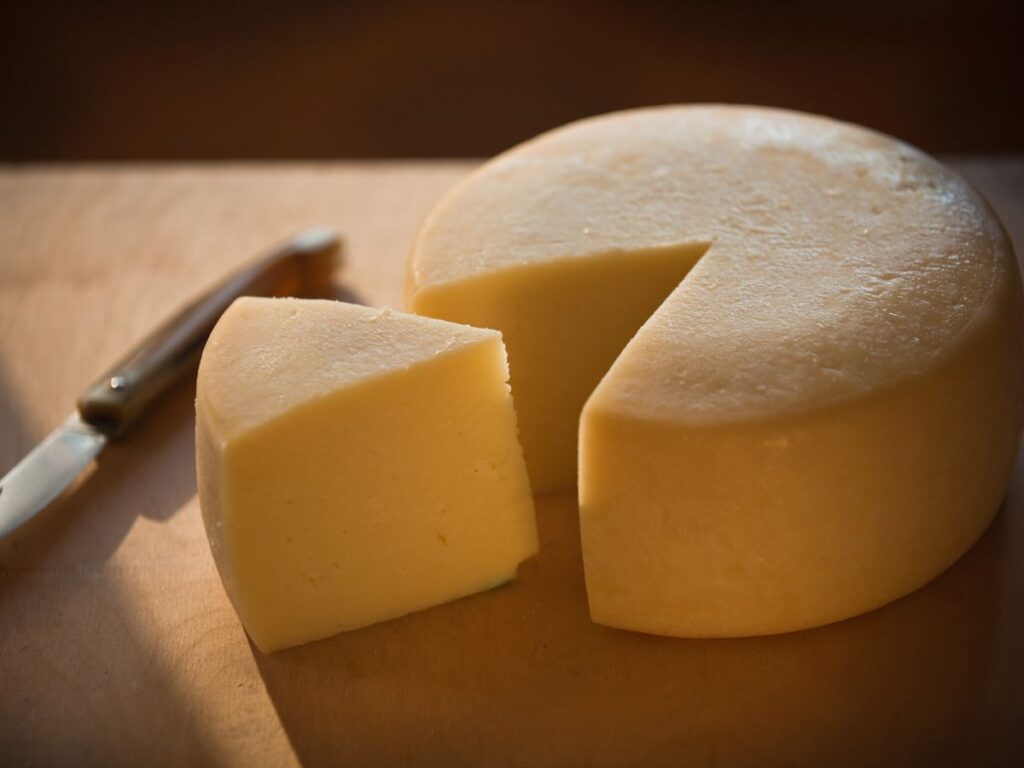 Forma di pecorino abbucciato del Casentino intera con una fetta tagliata su un tagliere di legno