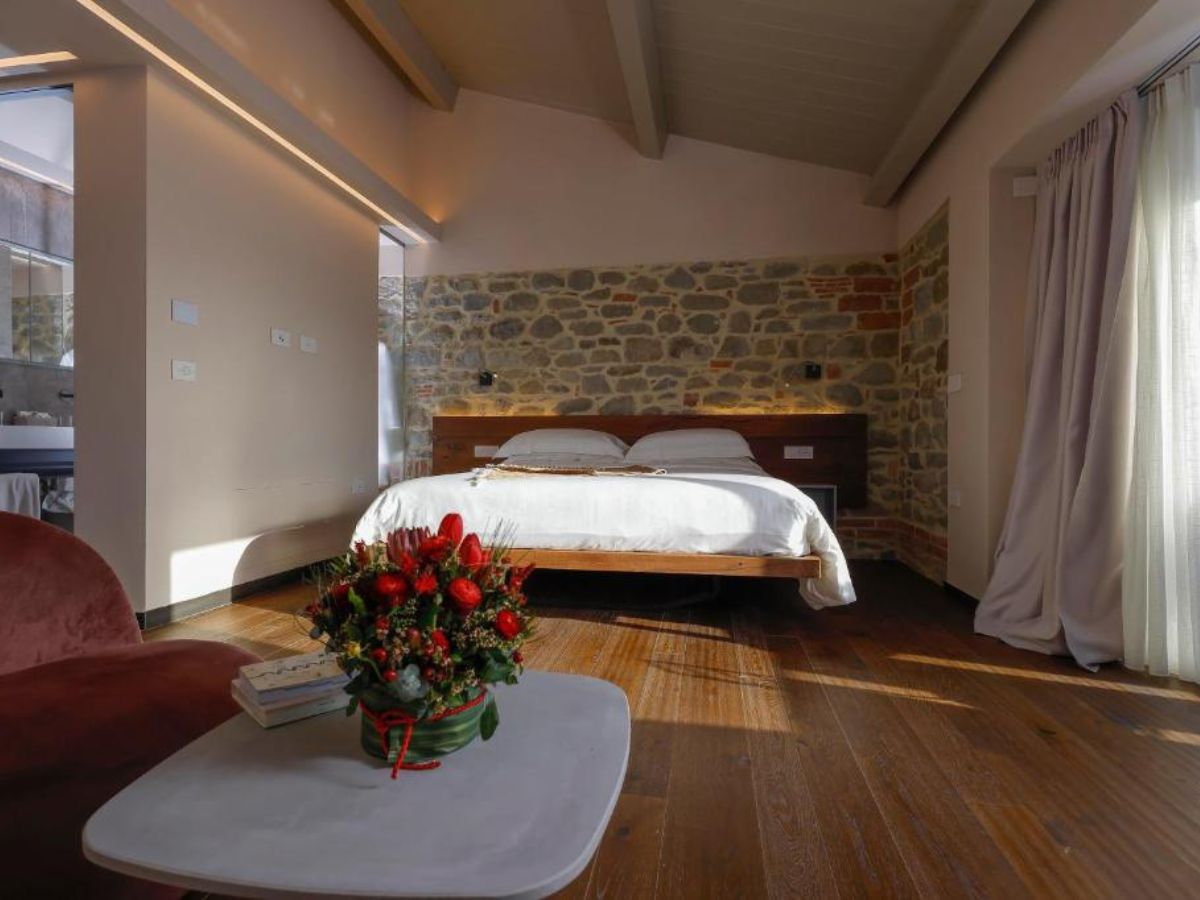 Camera da letto matrimoniale moderna con parete in pietra a vista, pavimento in legno e centro tavola floreale rosso.