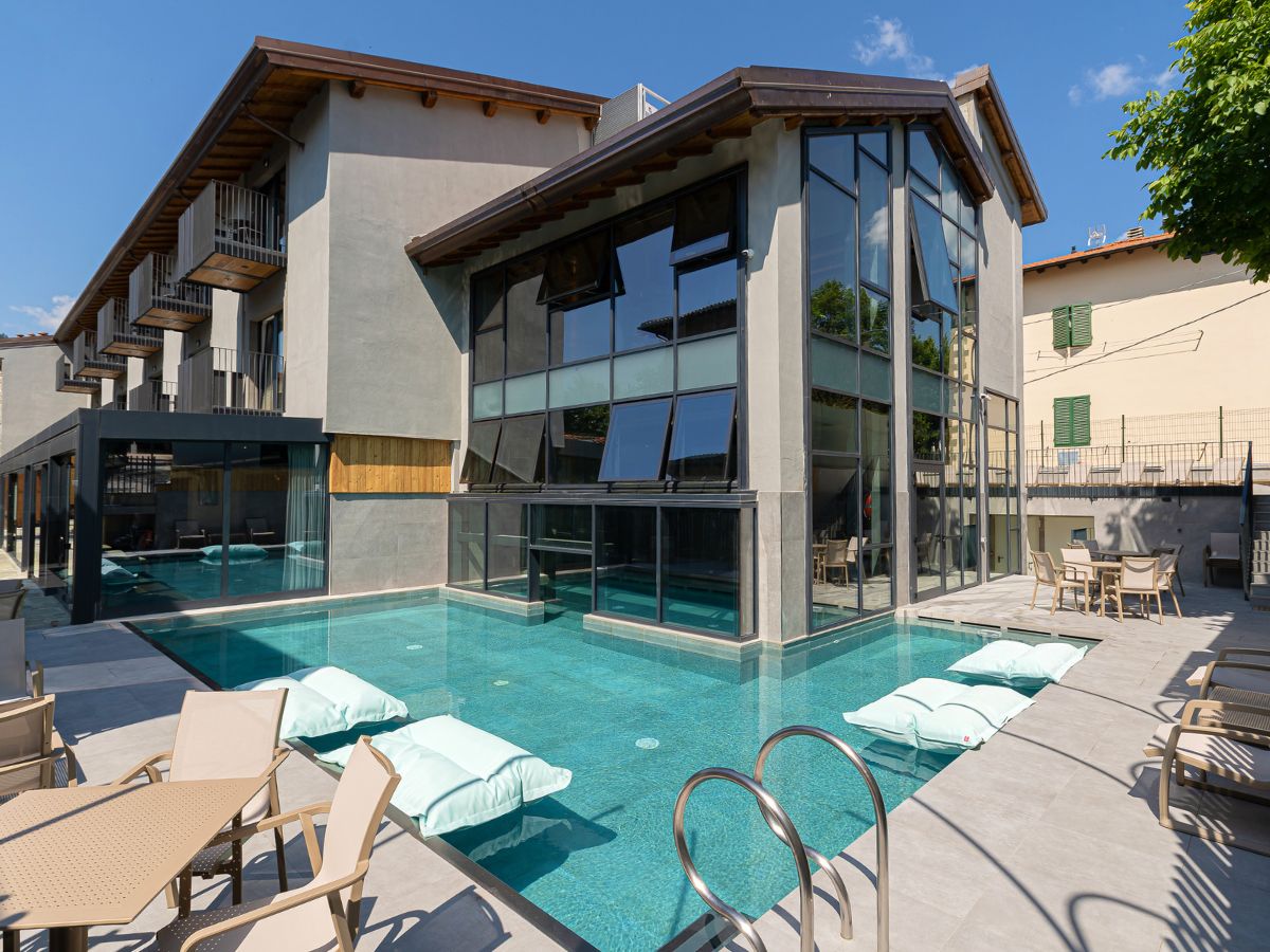 Piscina all'aperto di un hotel moderno con lettini galleggianti e vetrate panoramiche sulla struttura.