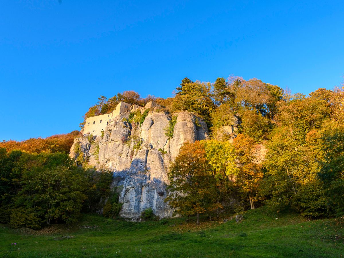 Scorcio del Santuario della Verna arroccato sulla roccia e circondato dagli alberi in veste autunnale sotto un cielo azzurro.