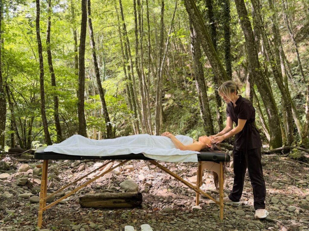Massaggio nel bosco di The Forest Experience: operatrice che massaggia il viso a un’ospite sdraiata tra gli alberi