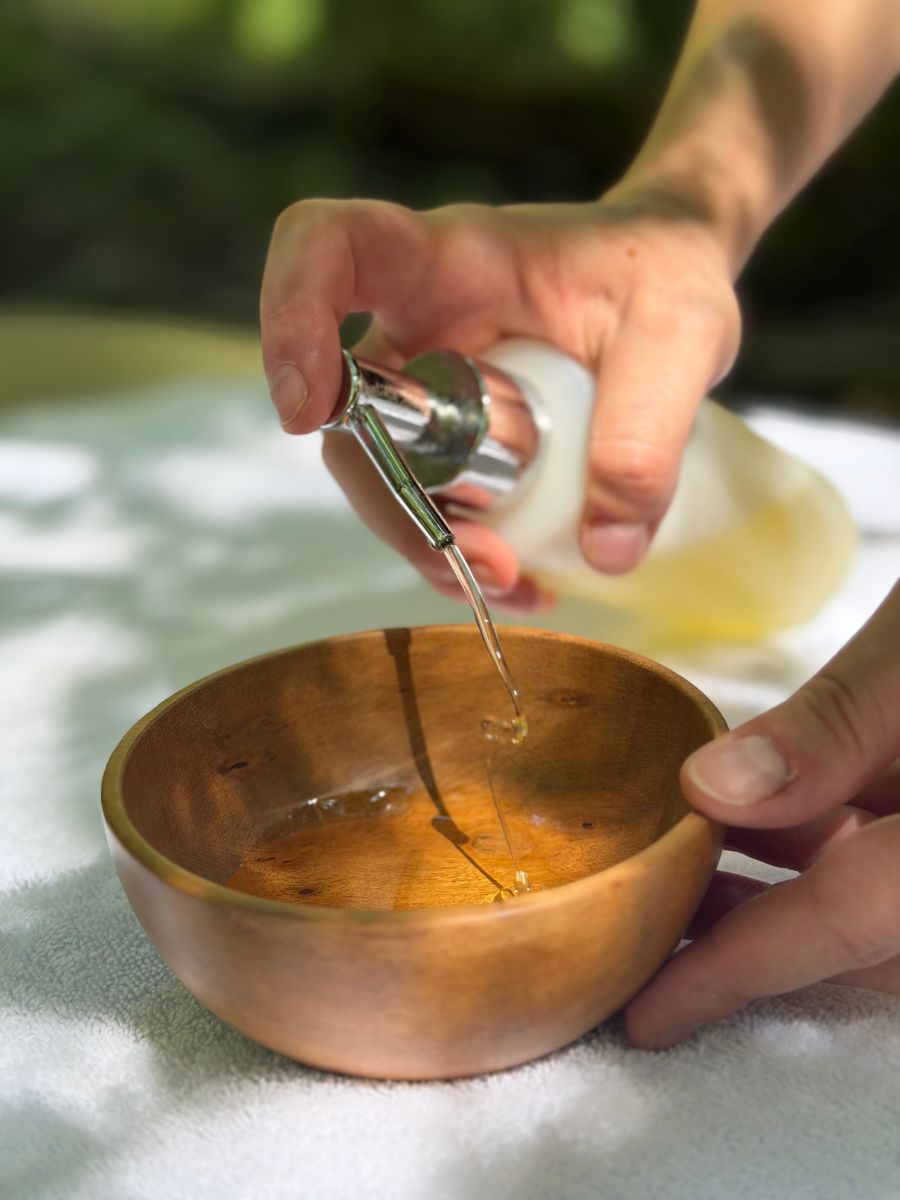 Olio da massaggio versato con un contagocce in una ciotola di legno durante il trattamento nel bosco