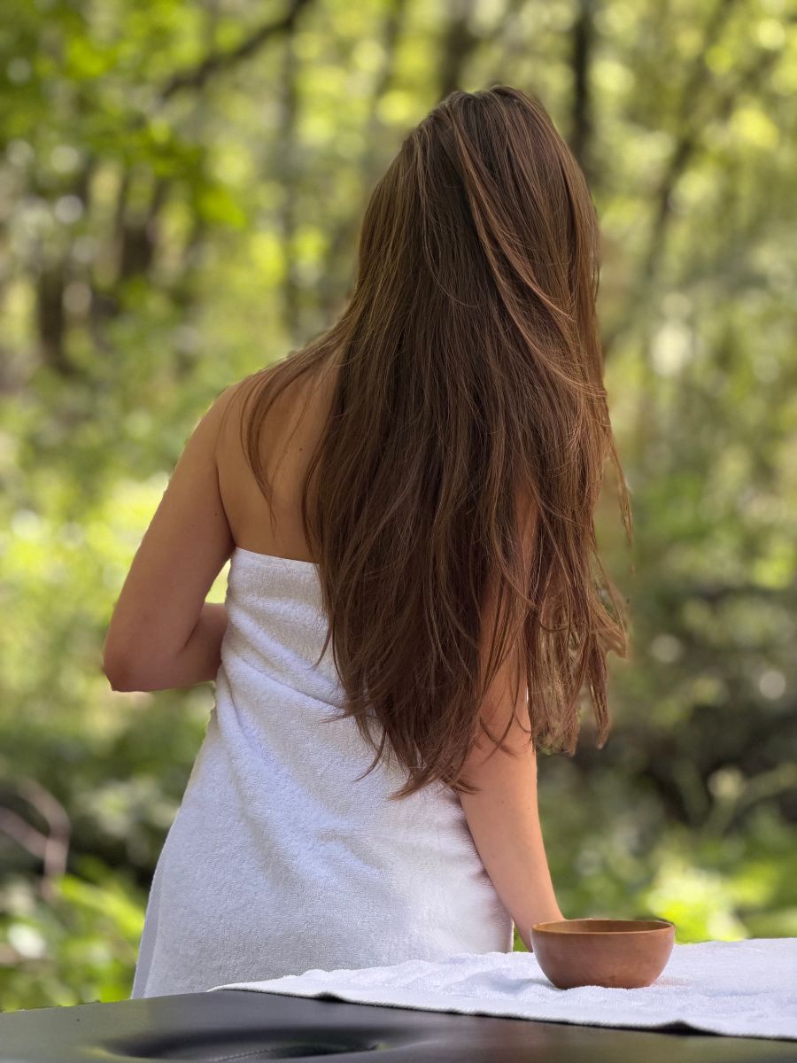 Ospite avvolta in un asciugamano bianco, di spalle, con il verde del bosco sullo sfondo